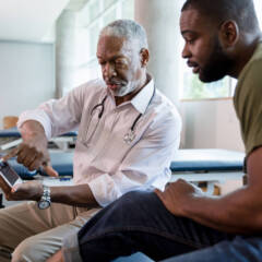 The mid adult male patient looks with interest as the mature adult male doctor points to the x-rays on the digital tablet screen.