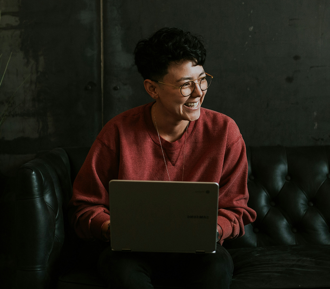 Woman on a couch smiling with her laptop open