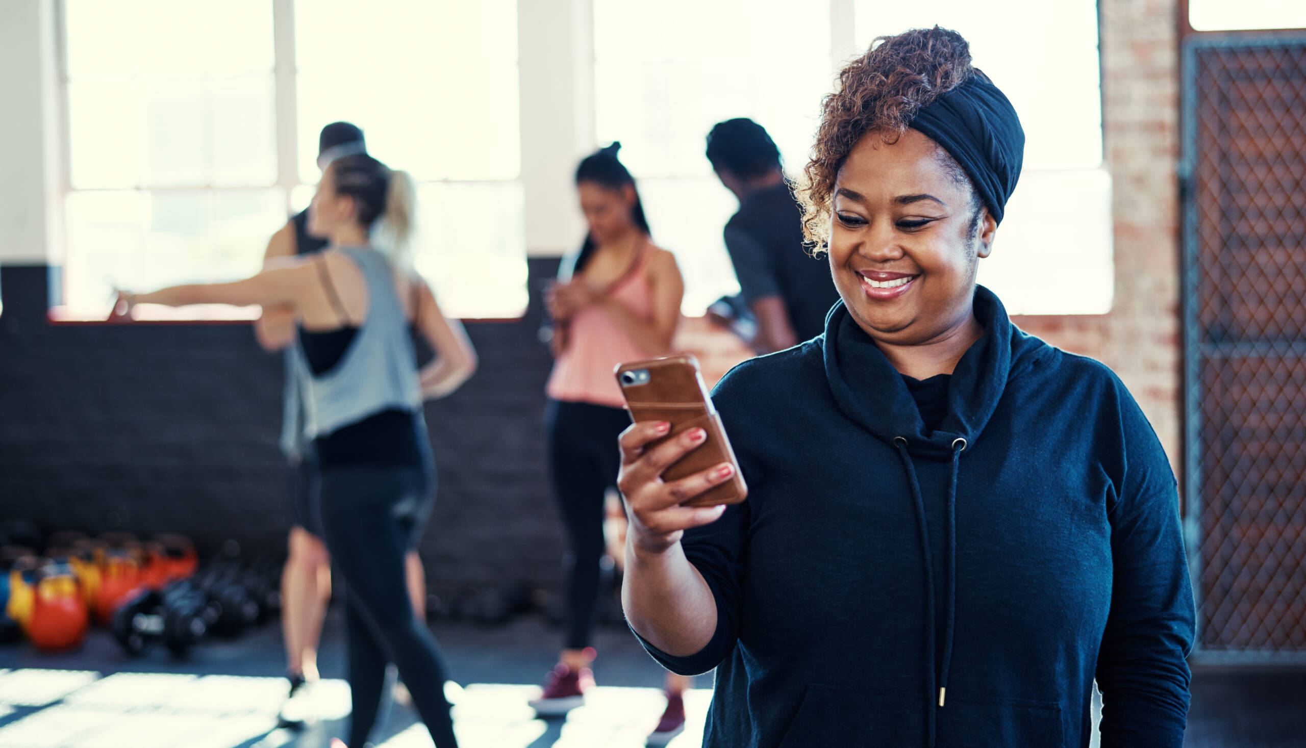 Shot of a cheerful young woman standing and using her cellphone before a workout session in a gym