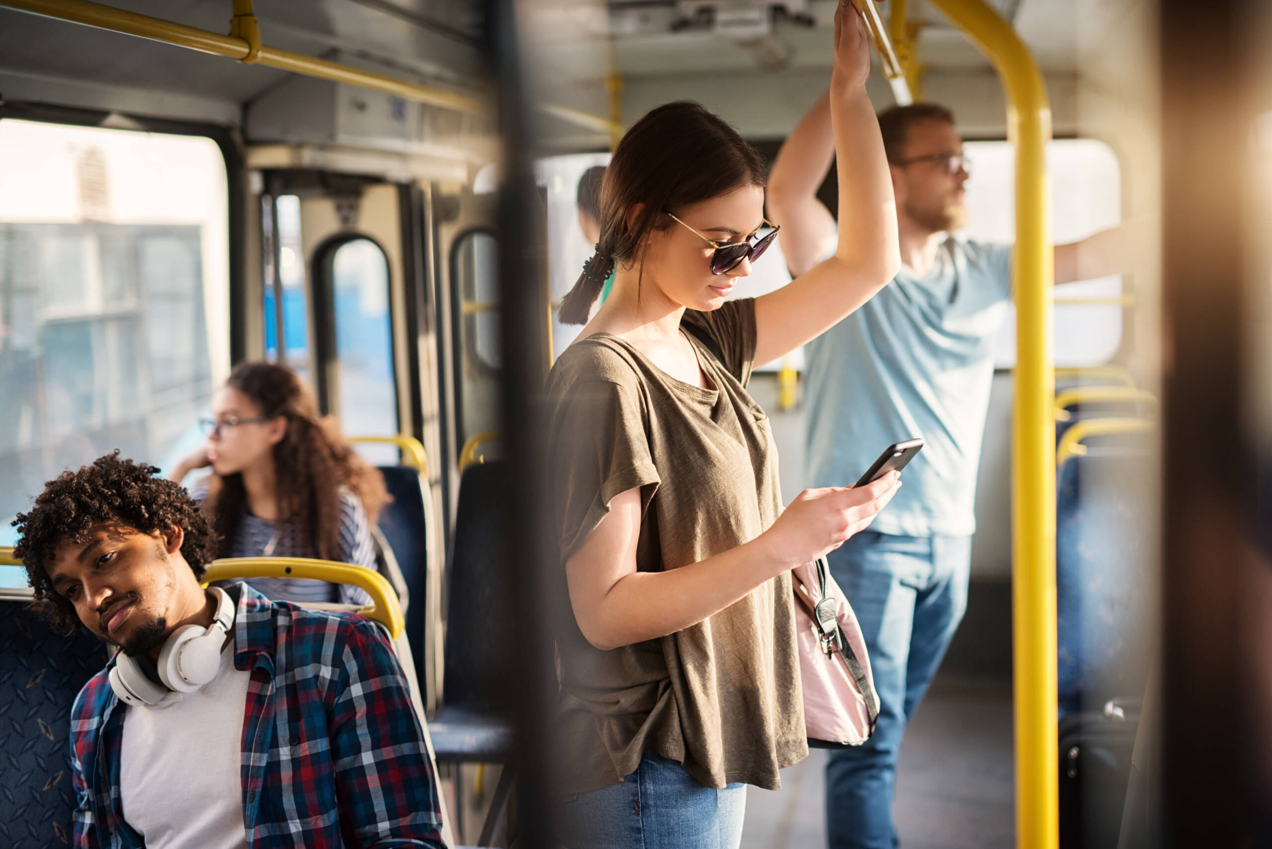 Girl with sunglasses in using phone while standing in a bus.