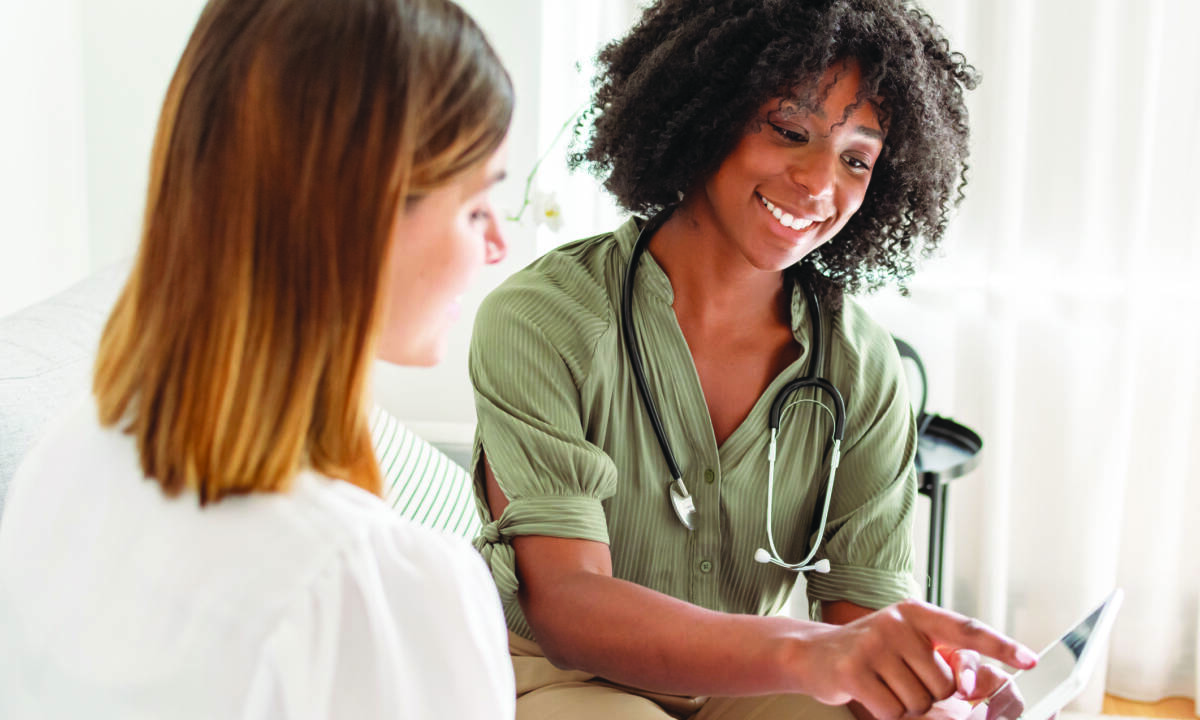 A young female doctor of African American descent smiles while reviewing test results on a tablet computer with a female patient during a medical appointment