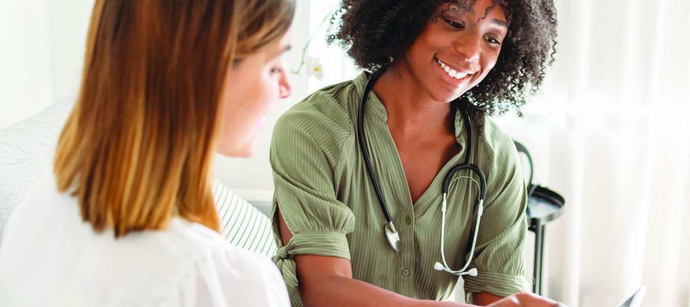 A young female doctor of African American descent smiles while reviewing test results on a tablet computer with a female patient during a medical appointment