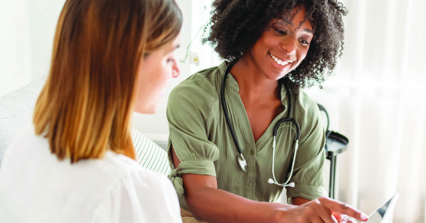 A young female doctor of African American descent smiles while reviewing test results on a tablet computer with a female patient during a medical appointment