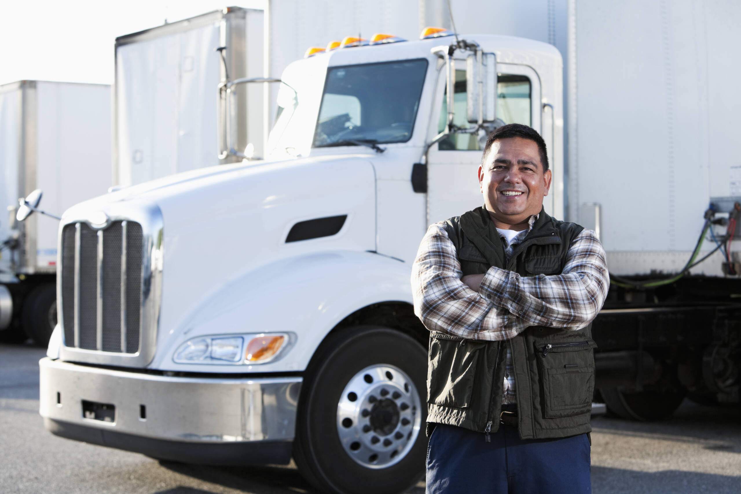 Hispanic truck driver (40s) standing in front of semi-truck.